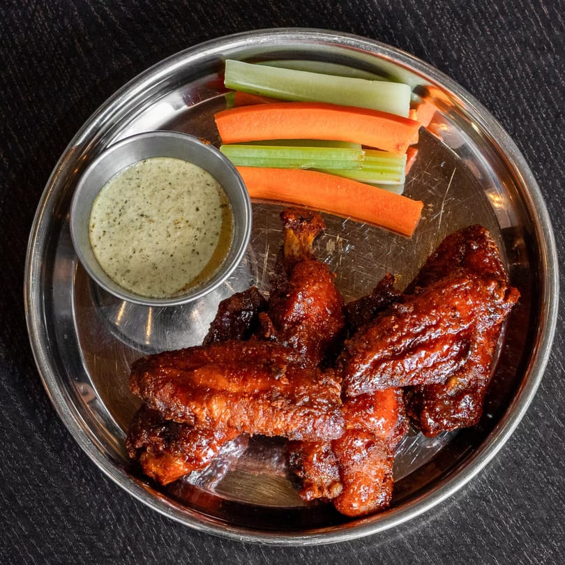 Mirchi Cafe's halal chicken wings, carrots, celery, and green dipping sauce on a metal plate.