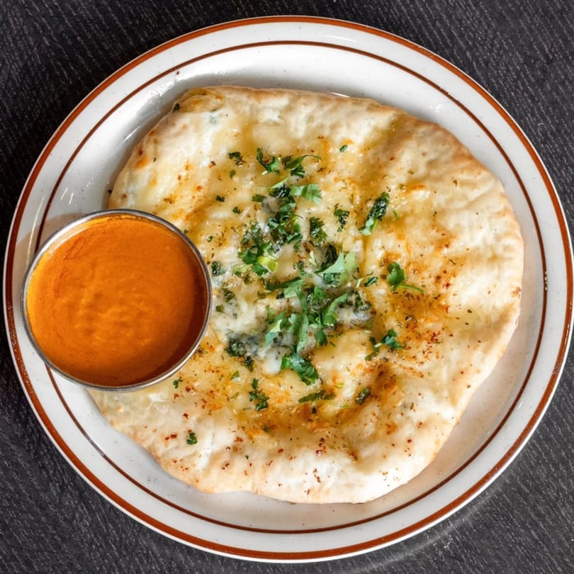 Garlic naan bread with fresh cilantro and a side of orange curry sauce on a white plate.