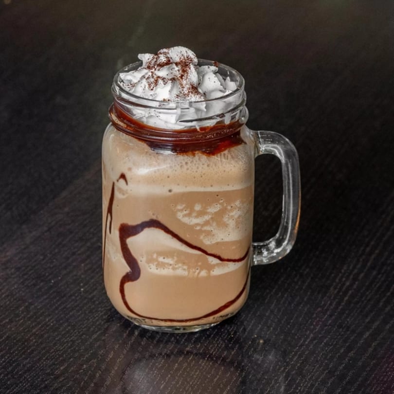 A Mirchi Cafe Masala Pizza frappe in a mason jar, topped with whipped cream and chocolate drizzle.