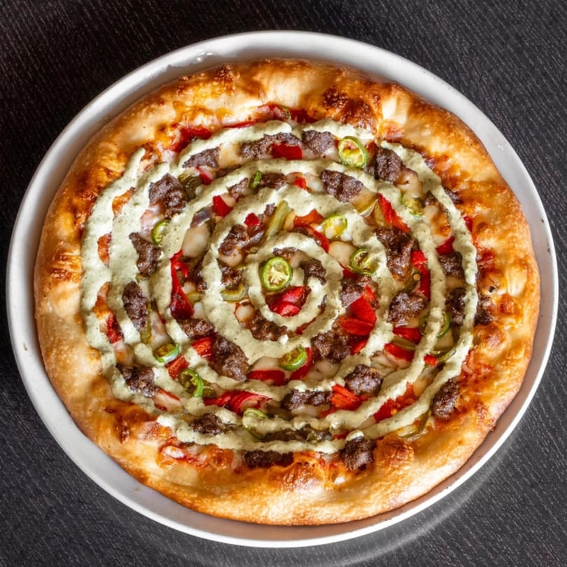 Halal Masala Pizza with ground meat, red peppers, green chilies, and a spiral of creamy sauce.