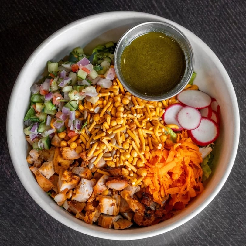 Mirchi Cafe's colorful salad with chicken, vegetables, crunchy toppings, and a side of dressing.